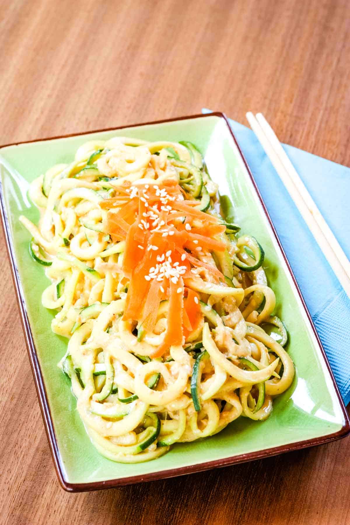 Sesame Peanut Zucchini Noodles on a green plate with wooden chopsticks on a blue napkin on the side.