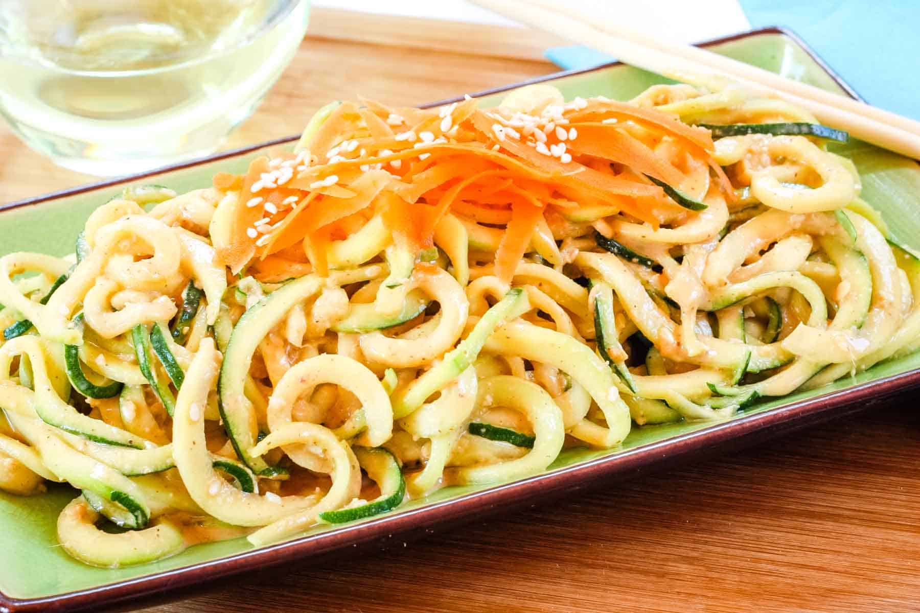 Cold Sesame Peanut Zucchini Noodles Salad topped with shredded carrots and sesame seeds on a green plate.