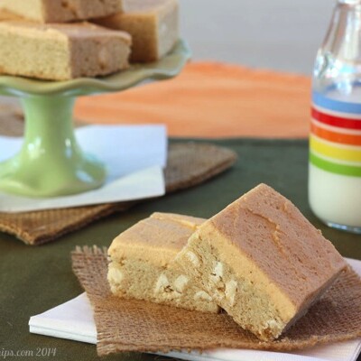 Frosted sugar cookie bars in the foreground, served next to a tall glass of milk.