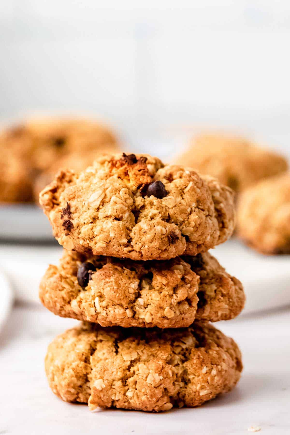 A stack of three trail mix cookies on a white countertop, with more cookies in the background.