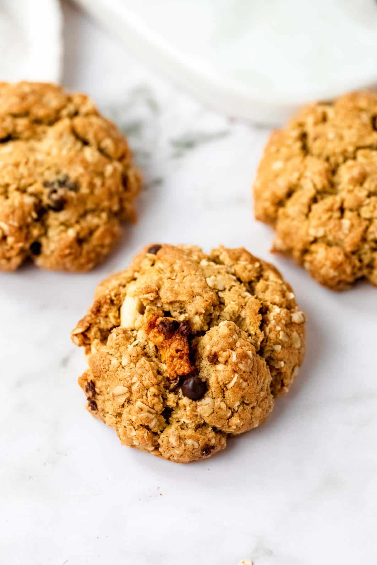 Three gluten-free trail mix cookies on a white marble countertop.