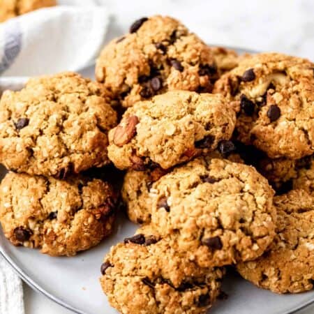 Assorted gluten-free trail mix cookies piled on a grey plate, on a white marble countertop.