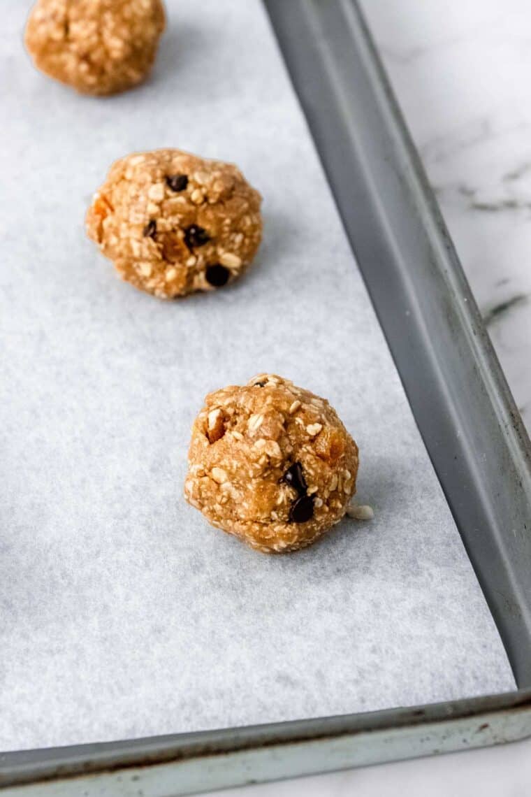 A row of three trail mix cookies on a parchment lined baking sheet.