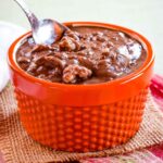Chocolate pumpkin oatmeal in a small orange bowl with a spoon in it.