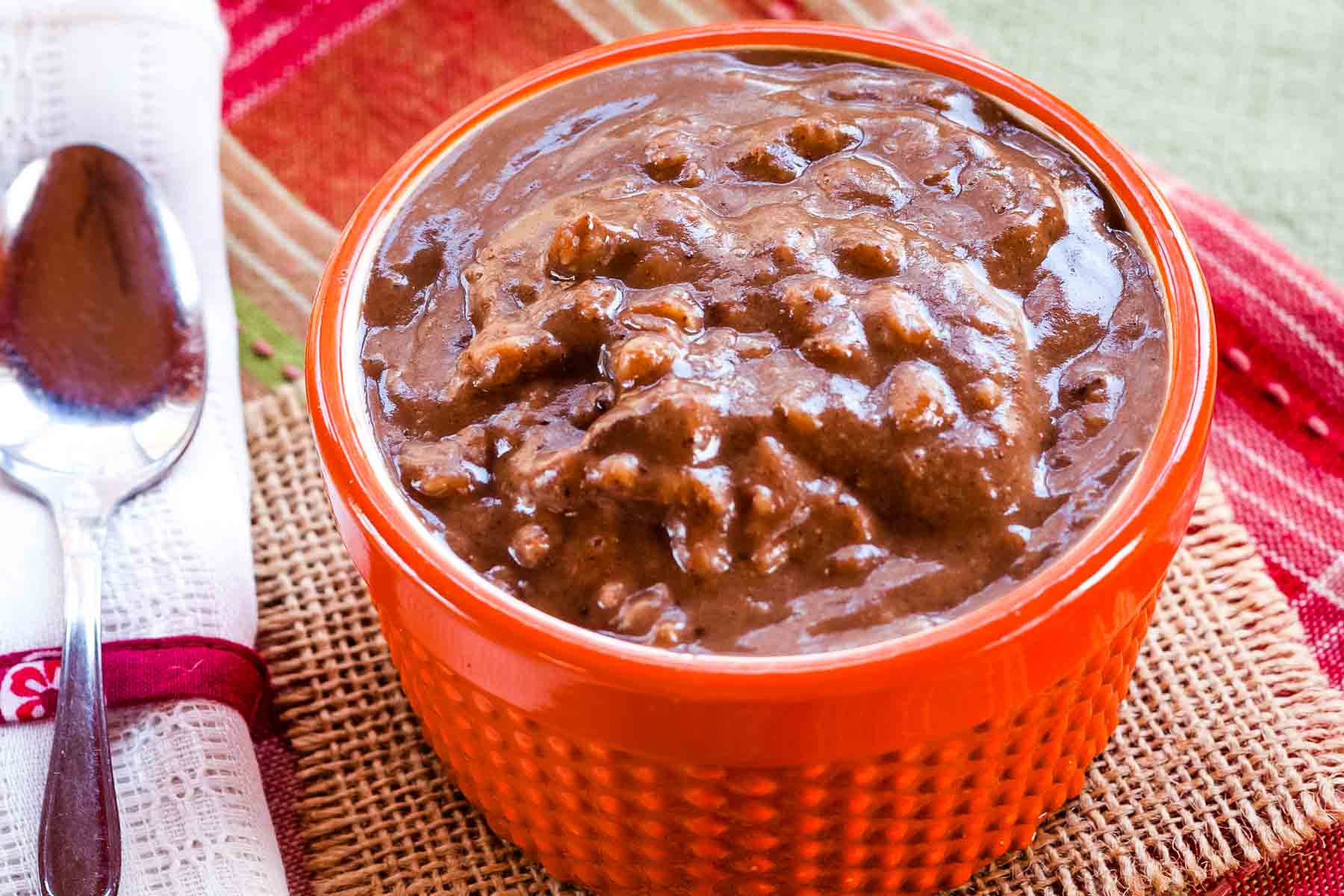 A bowl of pumpkin chocolate oatmeal and a spoon on a red and green plaid placemat.