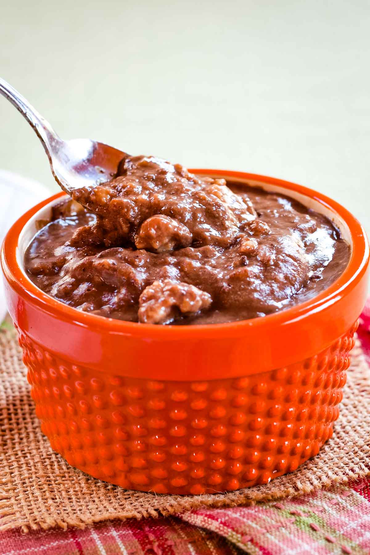 A spoon just set in chocolate pumpkin oatmeal that is in an orange textured ceramic bowl.