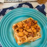 Apple cider waffles topped with caramelized apples on a blue plate.