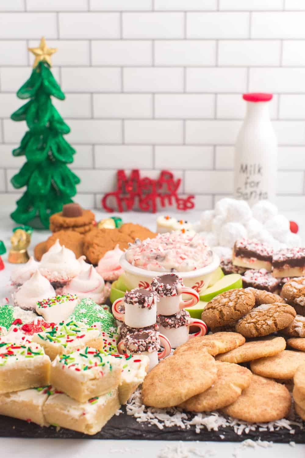 A slate platter piled with gluten free christmas cookies and candies with Christmas decorations in the background.