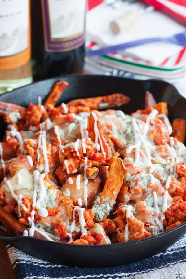 Sweet potato fries topped with buffalo chicken, blue cheese, and ranch in a cast iron skillet.