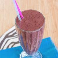 A purple-colored chocolate berry smoothie in a milkshake glass with two straws.