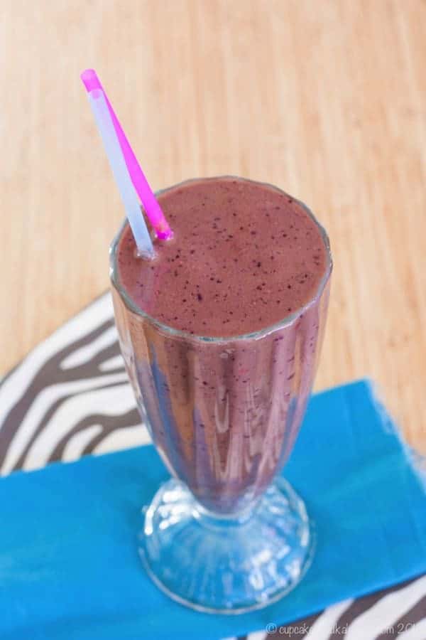 A purple-colored chocolate berry smoothie in a milkshake glass with two straws.