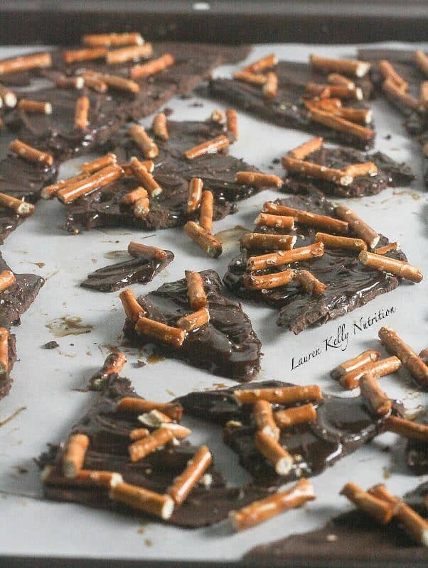 Chocolate bark with salted caramel and crushed pretzels arranged on parchment paper.