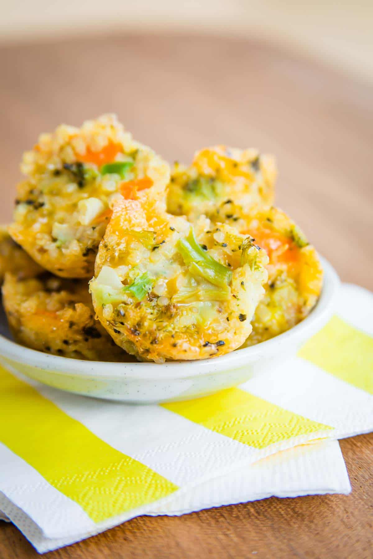 Cheesy Veggie Quinoa Bites in a small bowl on top of yellow and white napkins on a wooden tabletop.