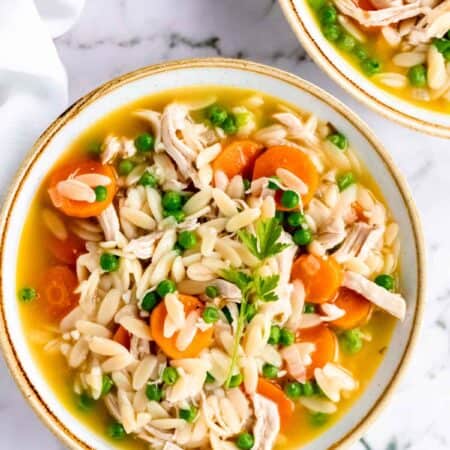 Overhead view of two bowls of gluten-free chicken orzo stew on a white marble countertop.