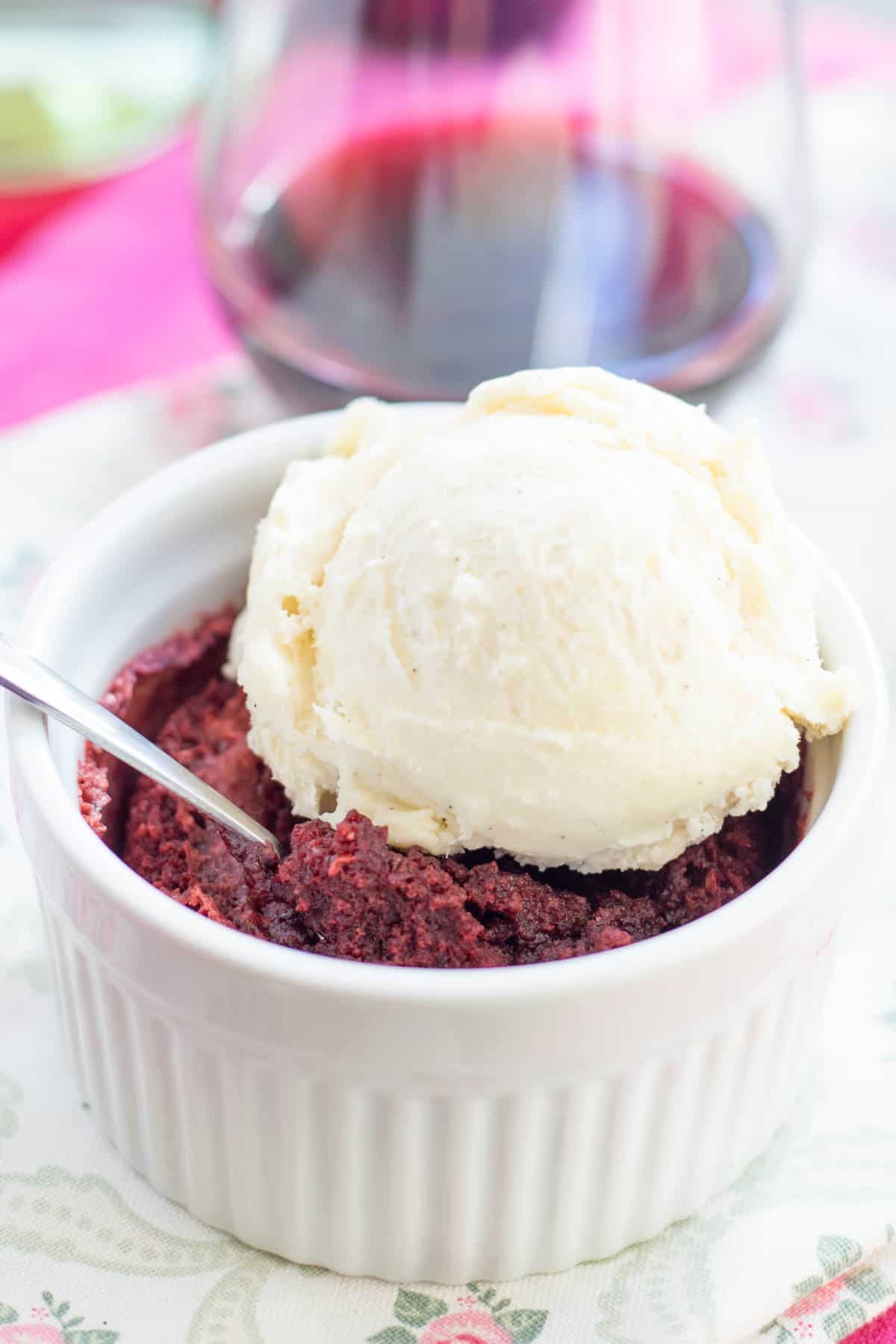 An ice cream-topped red velvet brownie in a ramekin with a spoon in it.