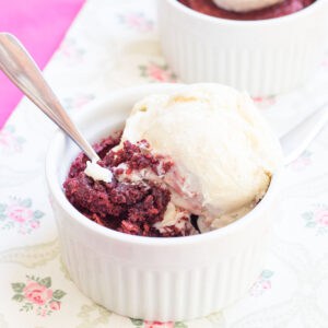 A spoon in a red velvet brownie in a ramekin topped with a melting scoop of vanilla ice cream.