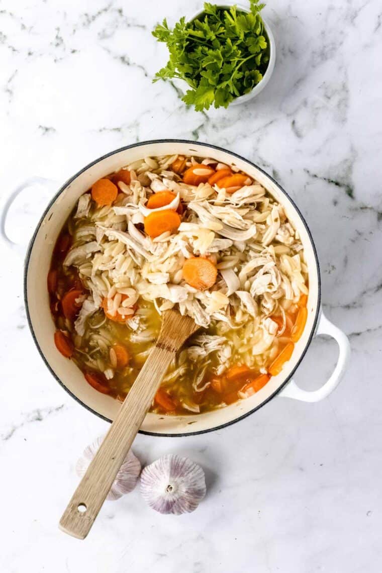 Chicken orzo stew ingredients inside a pot, stirred together with a wooden spoon.