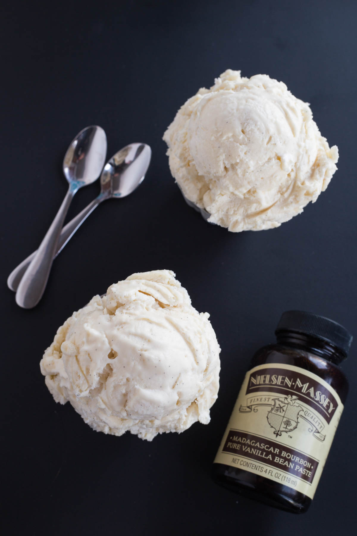 Looking down at two dishes of Vanilla Bean Cheesecake Ice Cream with a bottle of Nielsen-Massey Vanilla Bean Paste