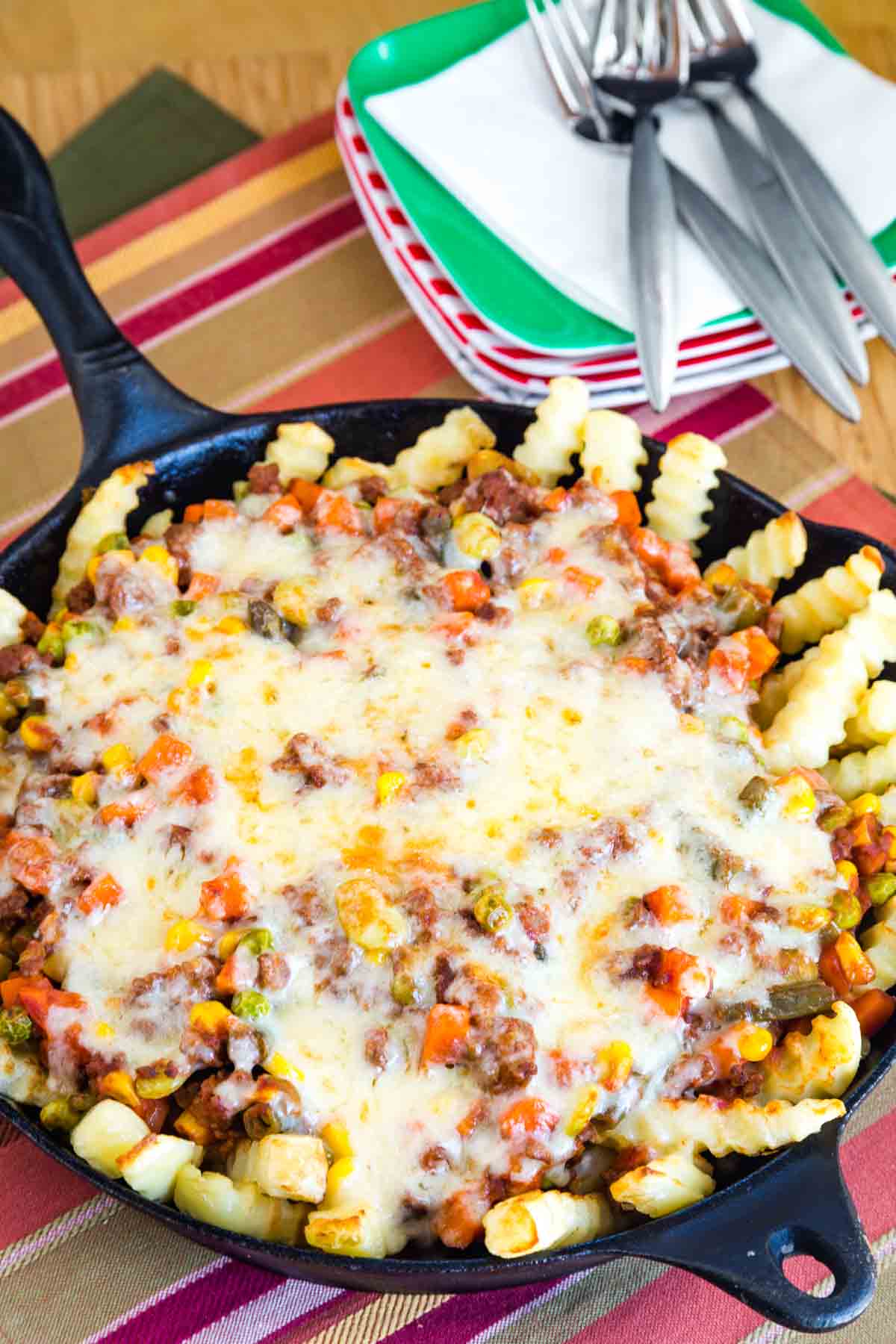 Overhead cast iron skillet with baked french fries topped with a shepherd's pie mixture of ground beef and mixed vegetables and melted cheddar cheese.
