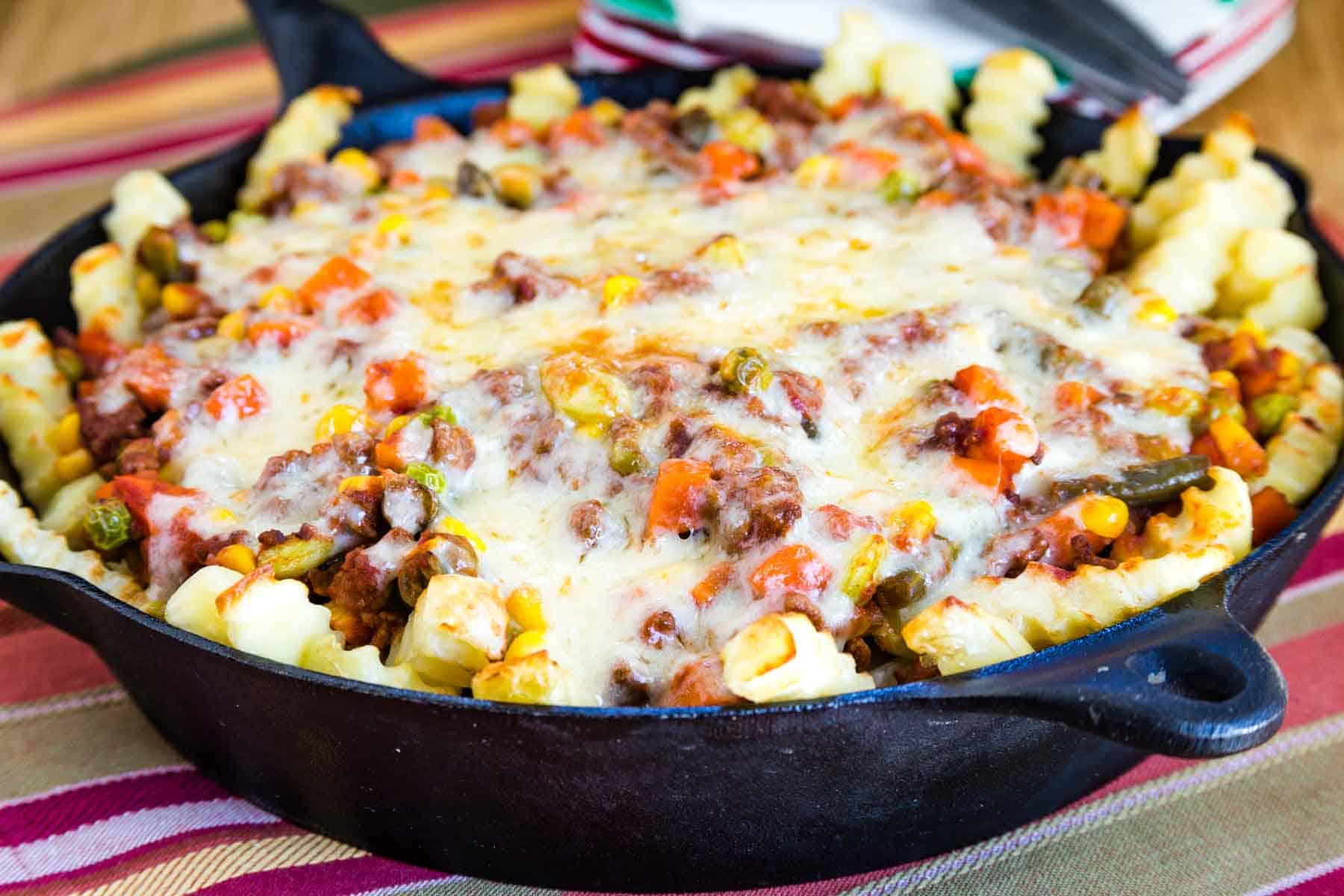 Cast Iron Skillet with Shepherd's Pie Ground Beef Loaded French Fries with cheese on top.