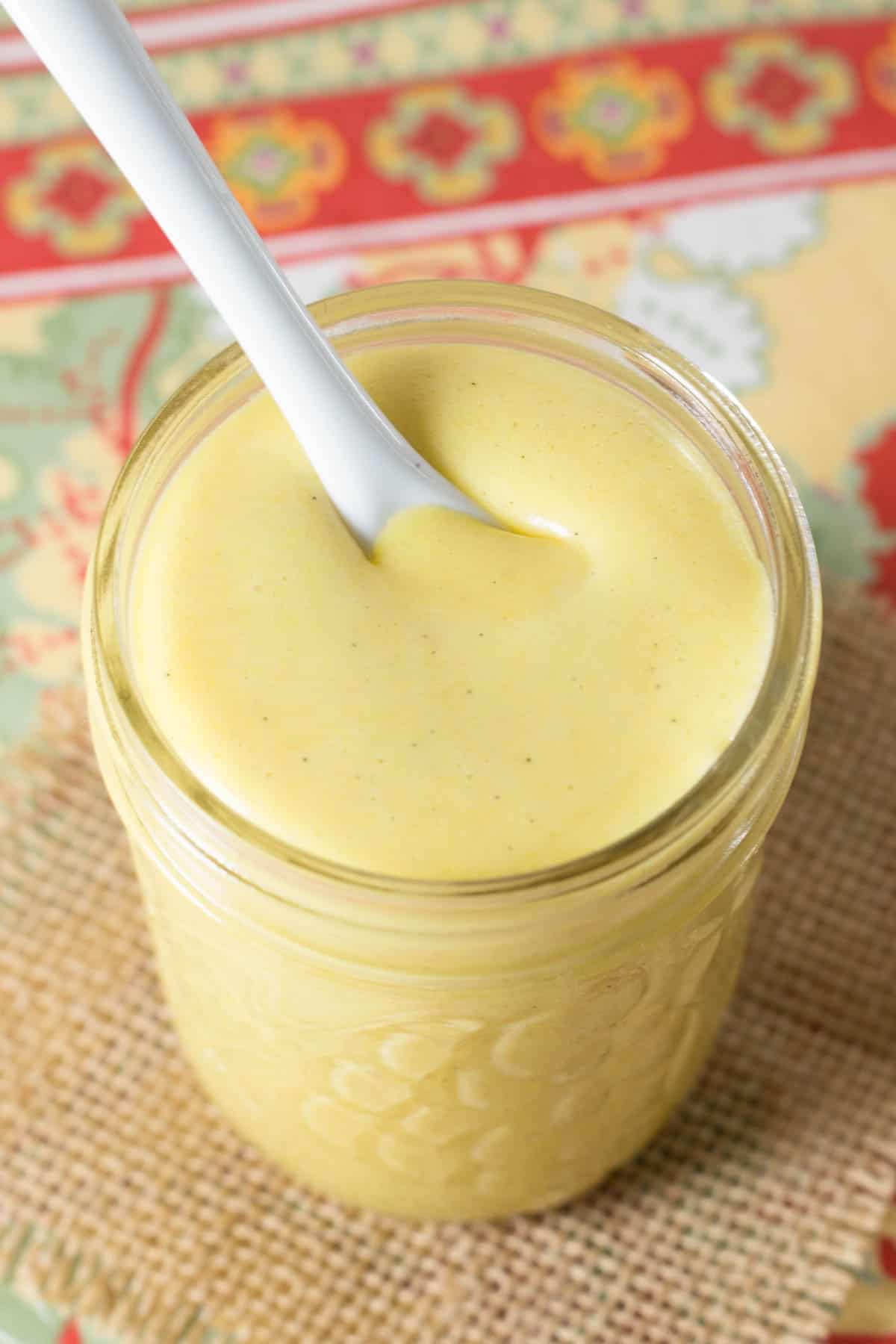 A white ceramic spoon resting in a glass jar of citrus curd.