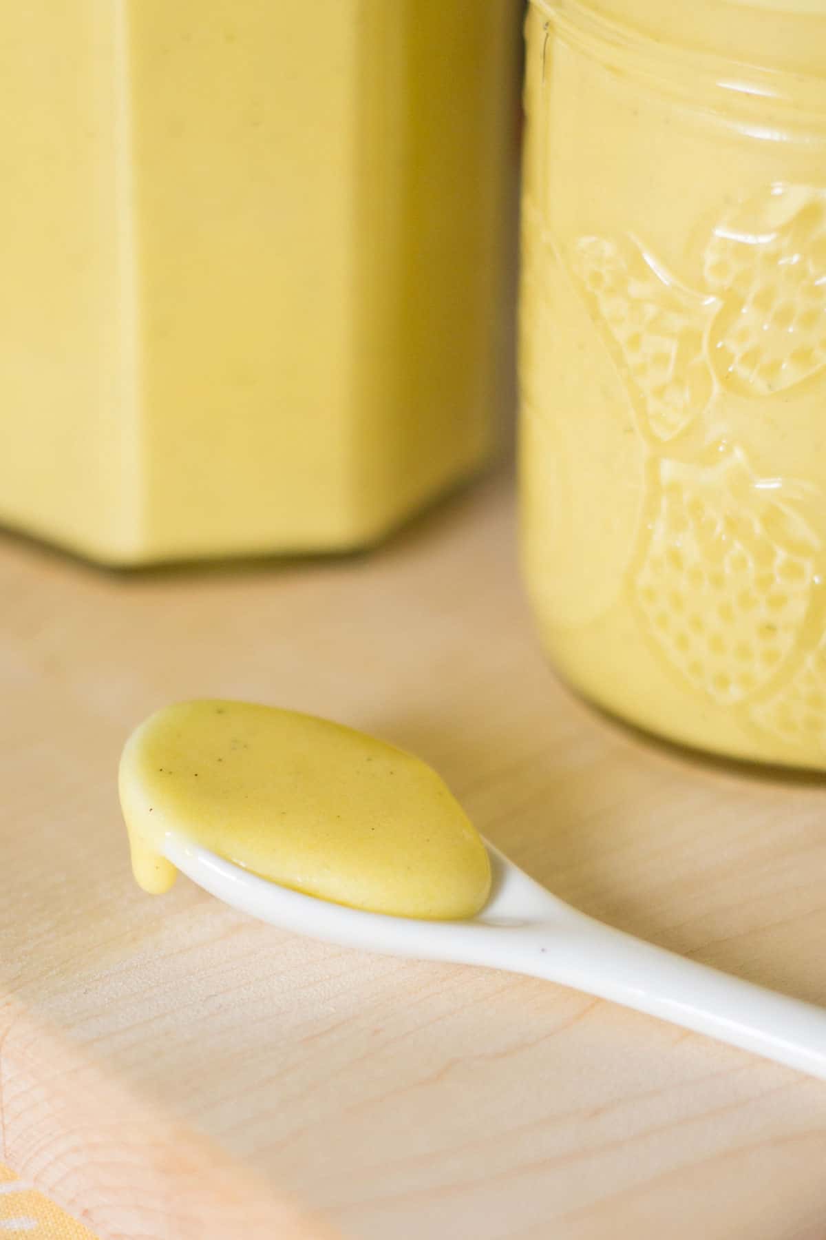 Thick yellow curd on a white spoon with two full jars of it behind the spoon.