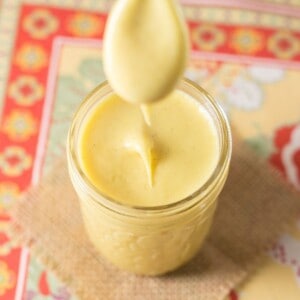 A jar of citrus curd with a spoon held above it with some dripping off.