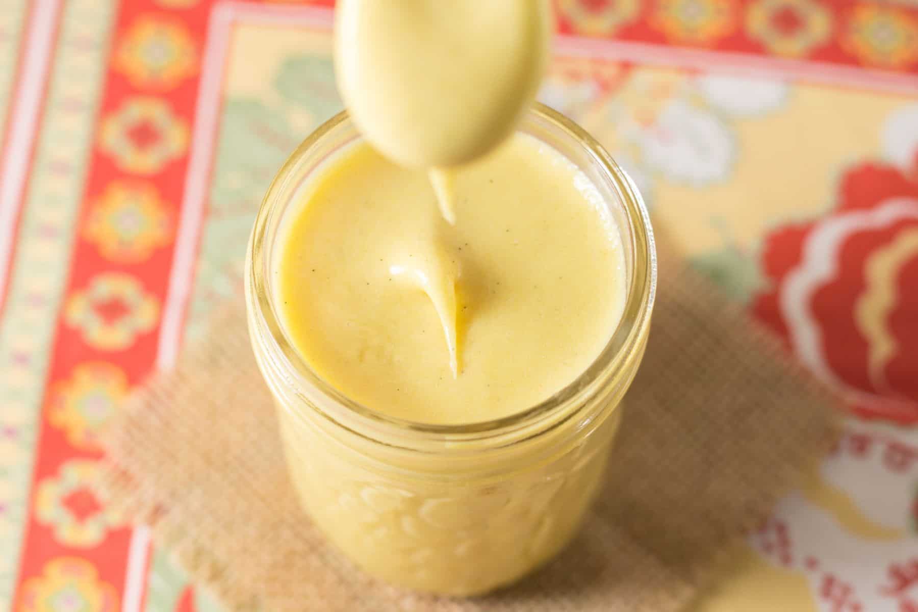 A jar of grapefruit curd with the tip of a spoon above it with some dripping off.