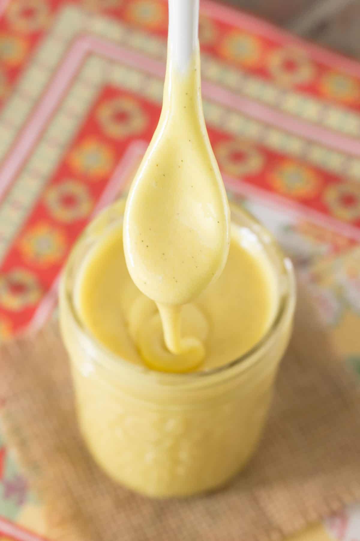 Grapefruit curd dripping off a white spoon into a glass jar.