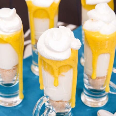 Creamsicle cheesecake parfaits on a turquoise cloth on a black table with some mini spoons.