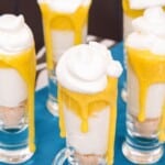 Mini desserts with layers of cheesecake and curd in small shot glasses with text overlay that says "Mini Creamsicle Parfaits".