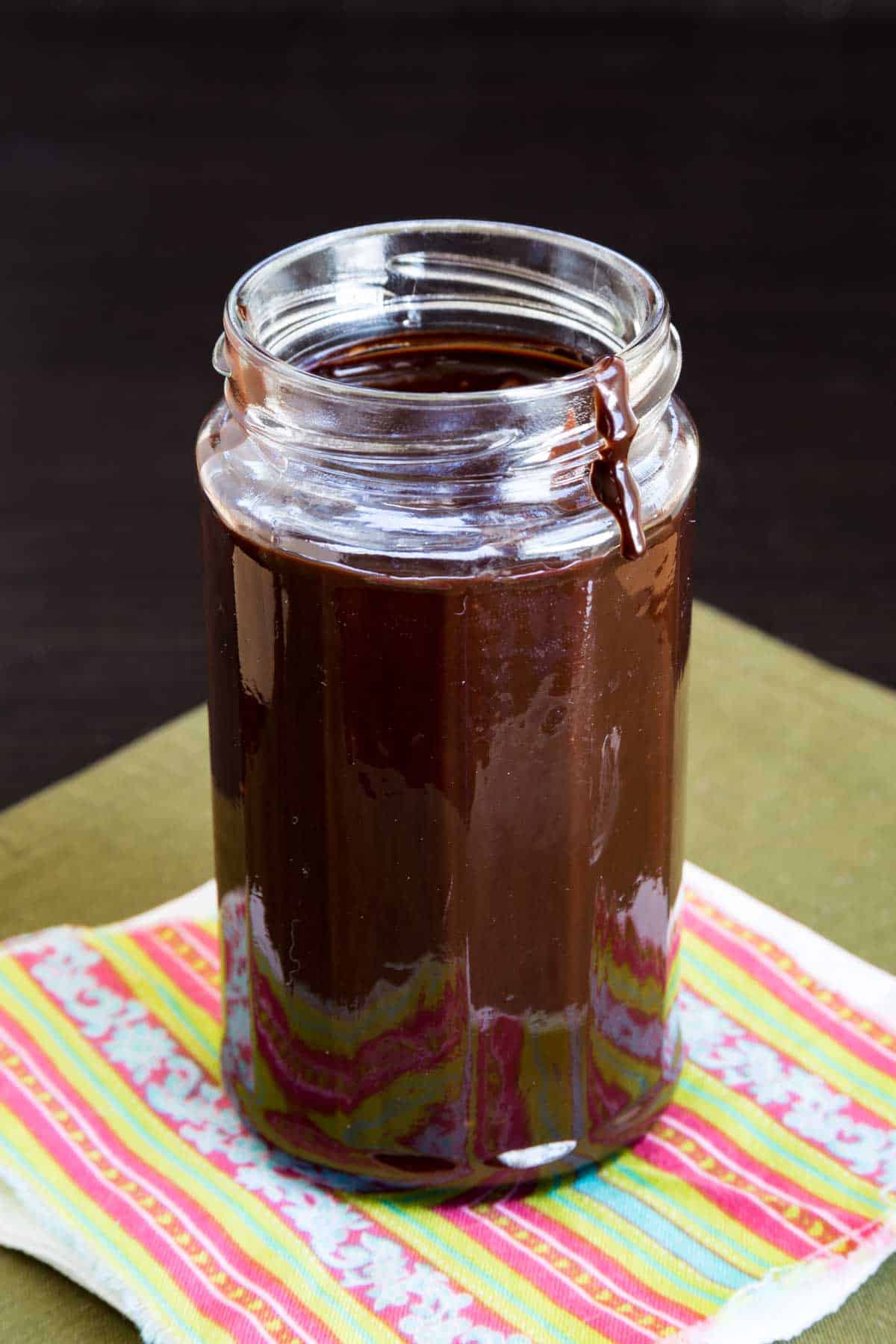 A jar of fudge sauce with a small drip on the lip of the jar.
