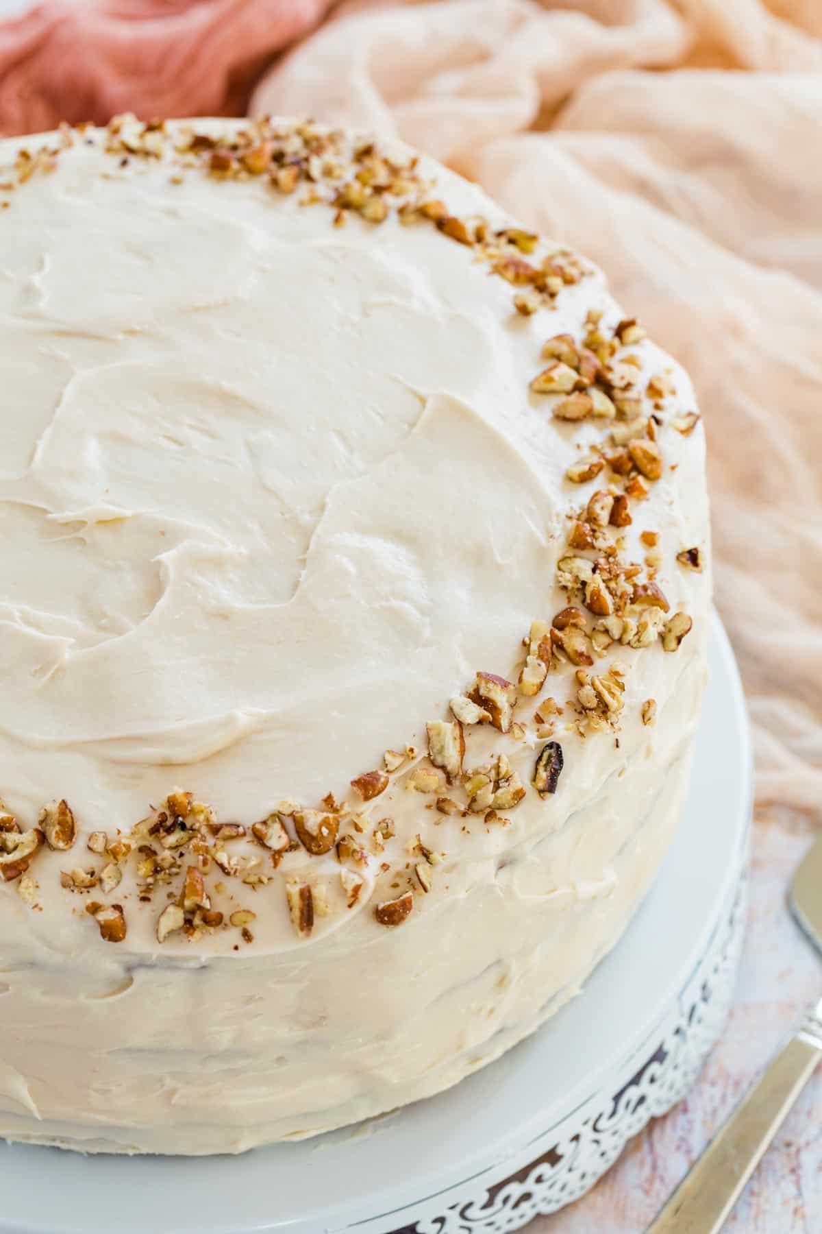 A full gluten free hummingbird cake on a plate, garnished with crushed pecans.