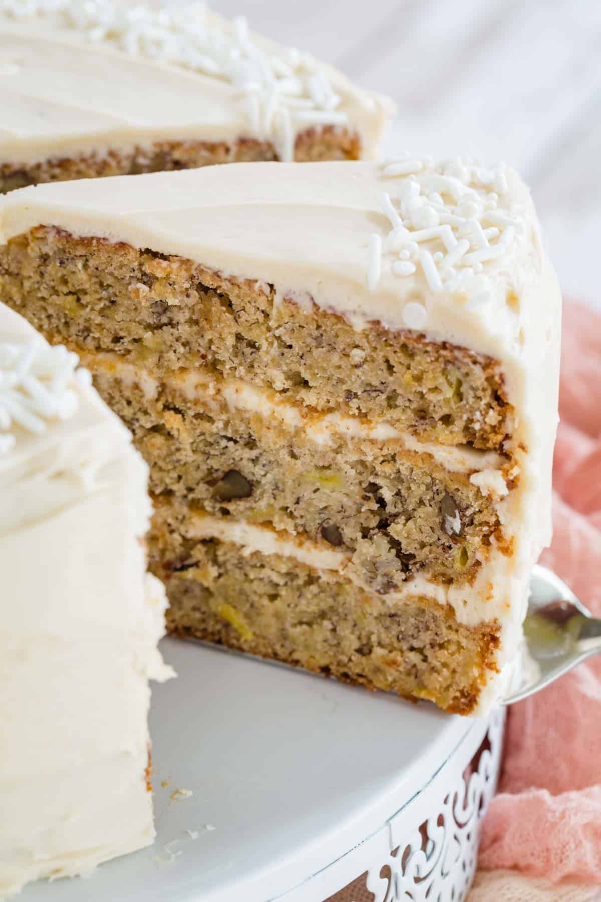 A slice of gluten free hummingbird cake is lifted from the rest of the cake.
