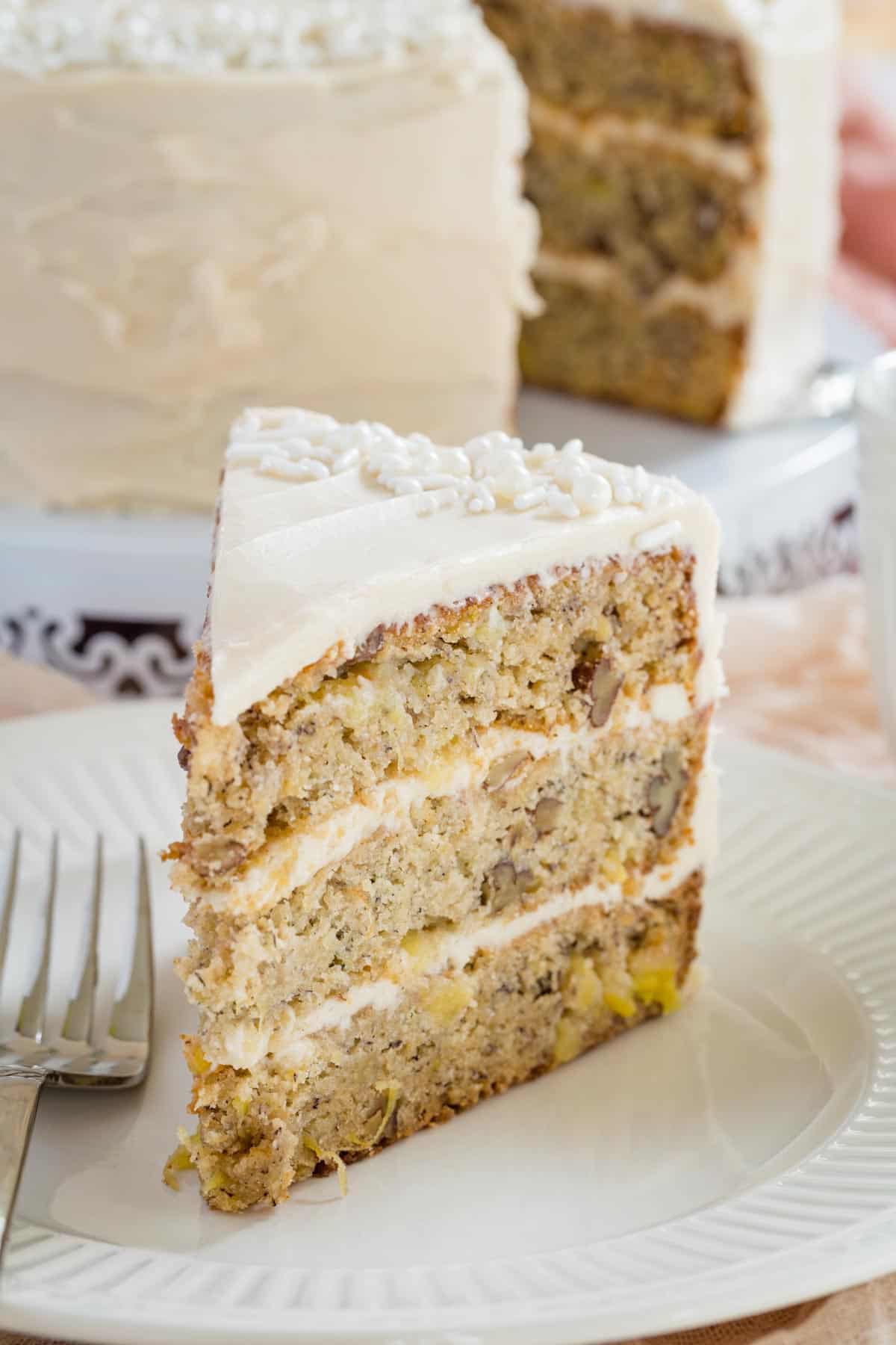 A slice of gluten free hummingbird cake on a plate next to a fork.