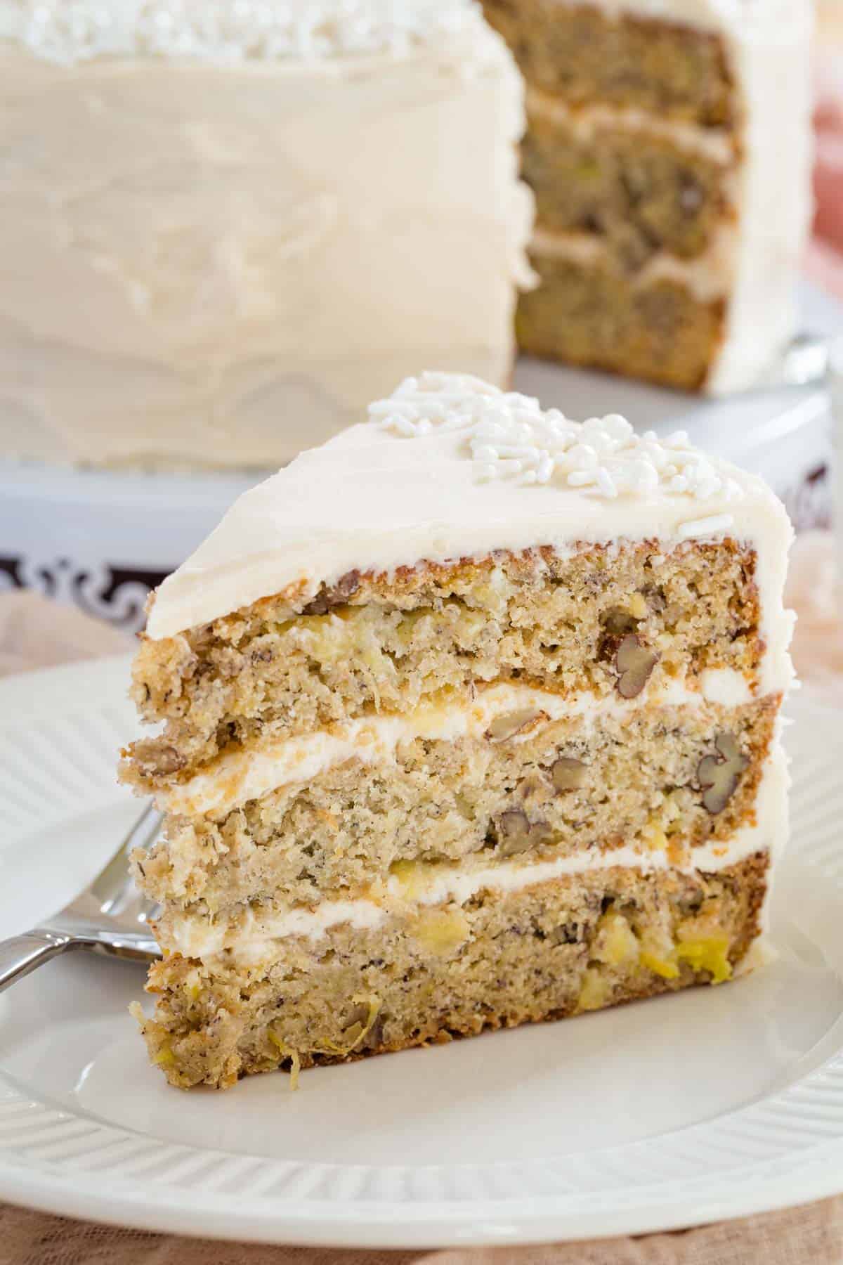 A slice of gluten free hummingbird cake on a plate next to a fork.