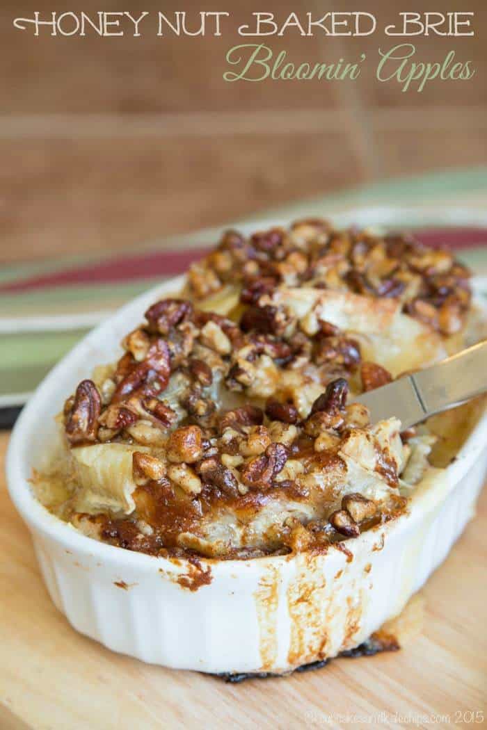 A cheese knife cuts into Honey Nut Baked Brie Bloomin' Apples served in a baking dish