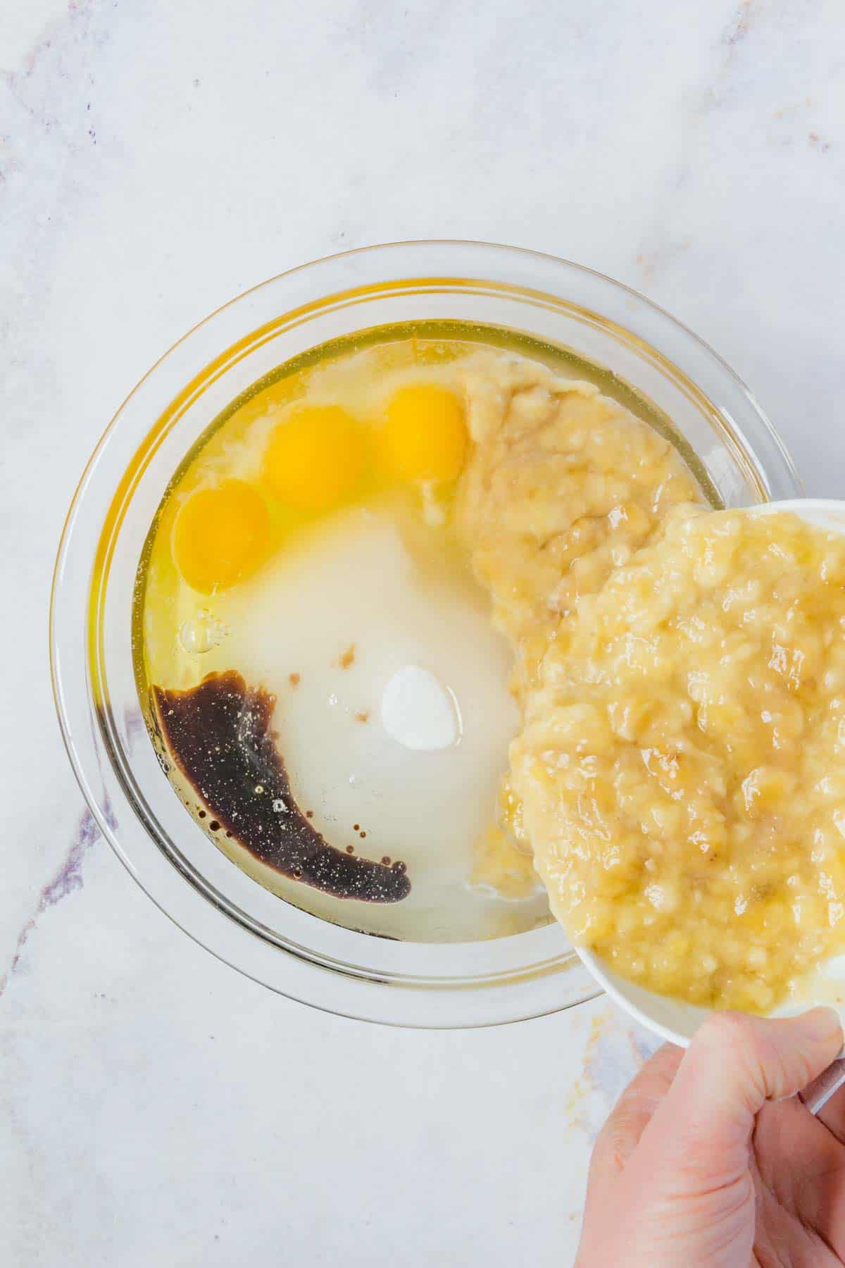 The bananas are added into the wet ingredients in a mixing bowl.