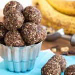 Chunky Monkey Energy Balls in a silver cup with bananas, walnuts, and chocolate chunks in the background