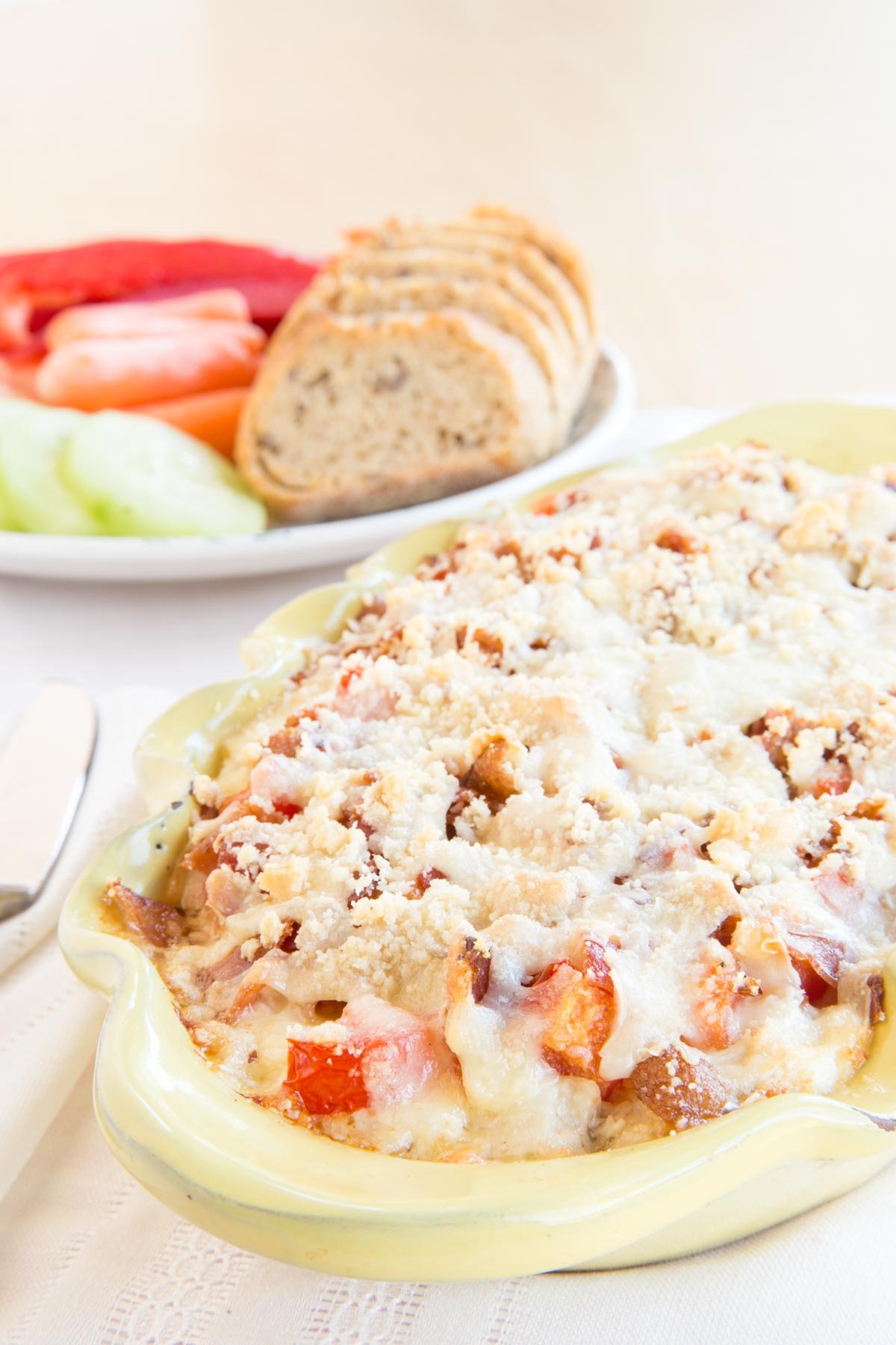 Yellow dish with Ketucky Hot Brown Dip and a plate of veggies and baguette slices next to it