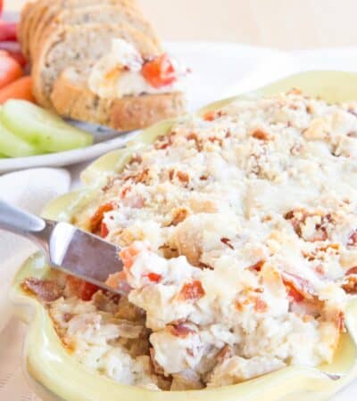 Hot turkey and cheese dip with bacon in a pale yellow casserole dish being scooped up with a knife