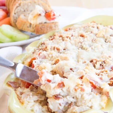 Hot turkey and cheese dip with bacon in a pale yellow casserole dish being scooped up with a knife