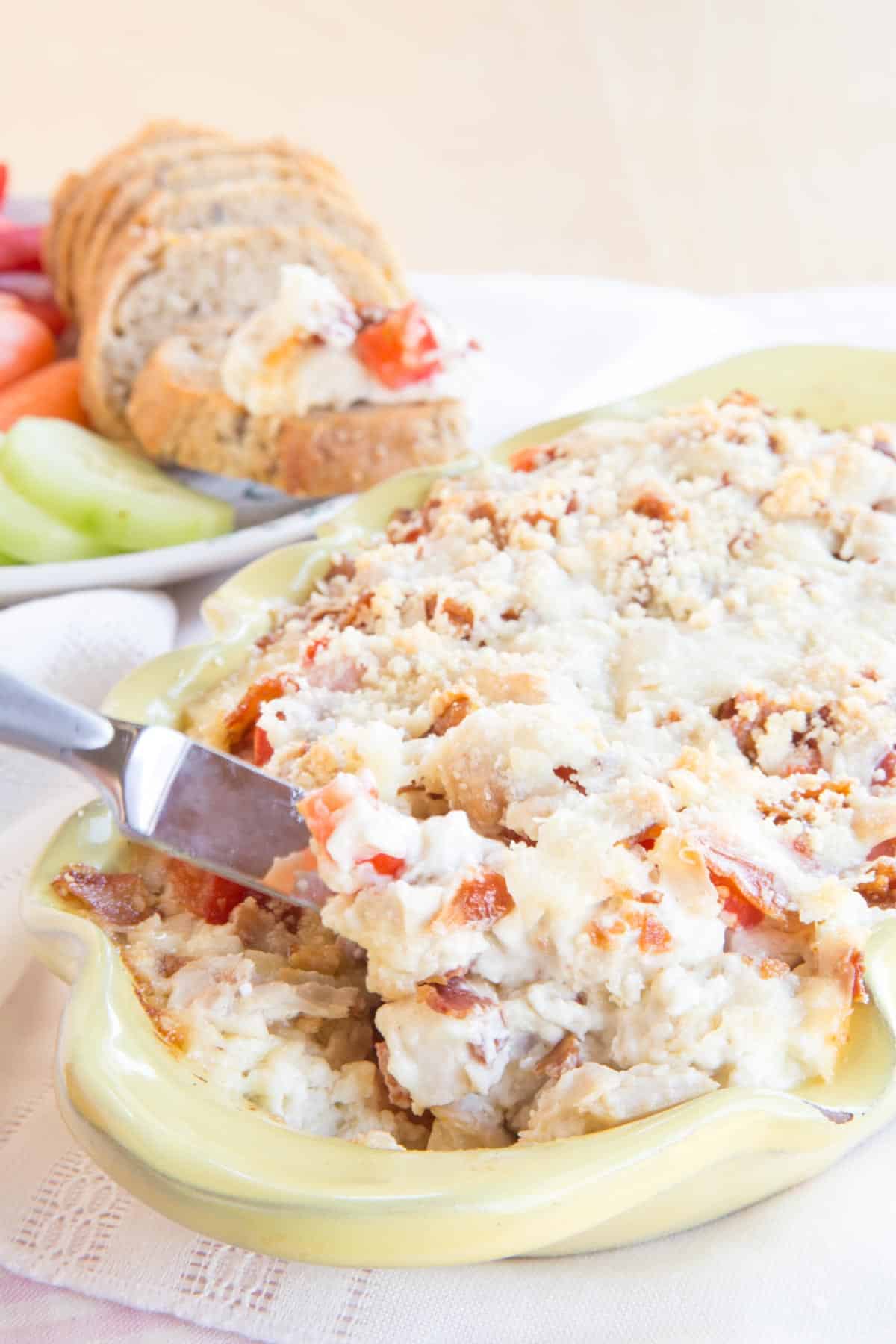 Hot turkey and cheese dip with bacon in a pale yellow casserole dish being scooped up with a knife