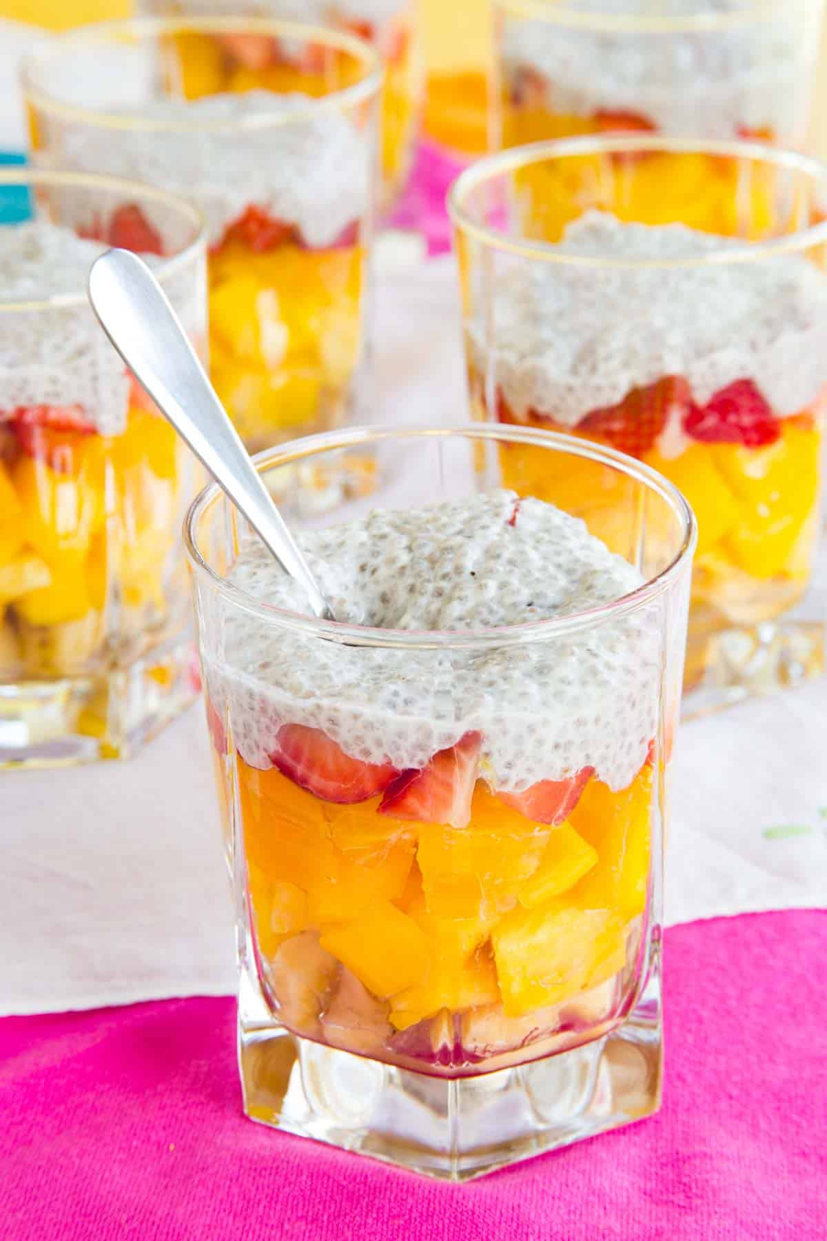A spoon in a glass of tropical fruit salad with coconut cream on top.