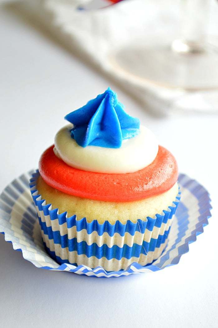 Lemon cupcake with layers of red, white, and blue frosting and a blue and white striped liner