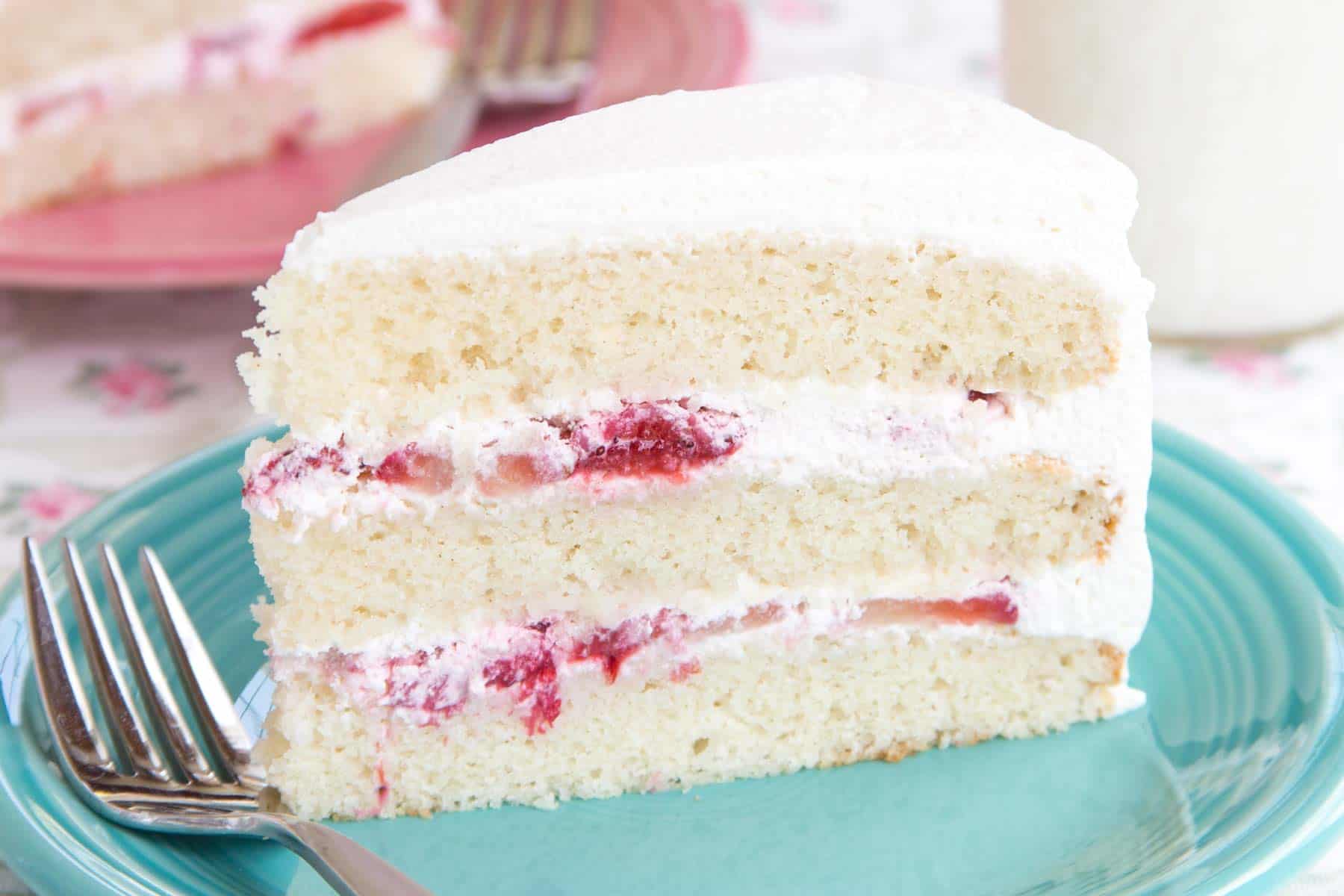 A side view of a piece of gluten free cake to see the layers of white cake, fresh strawberries, and whipped cream.