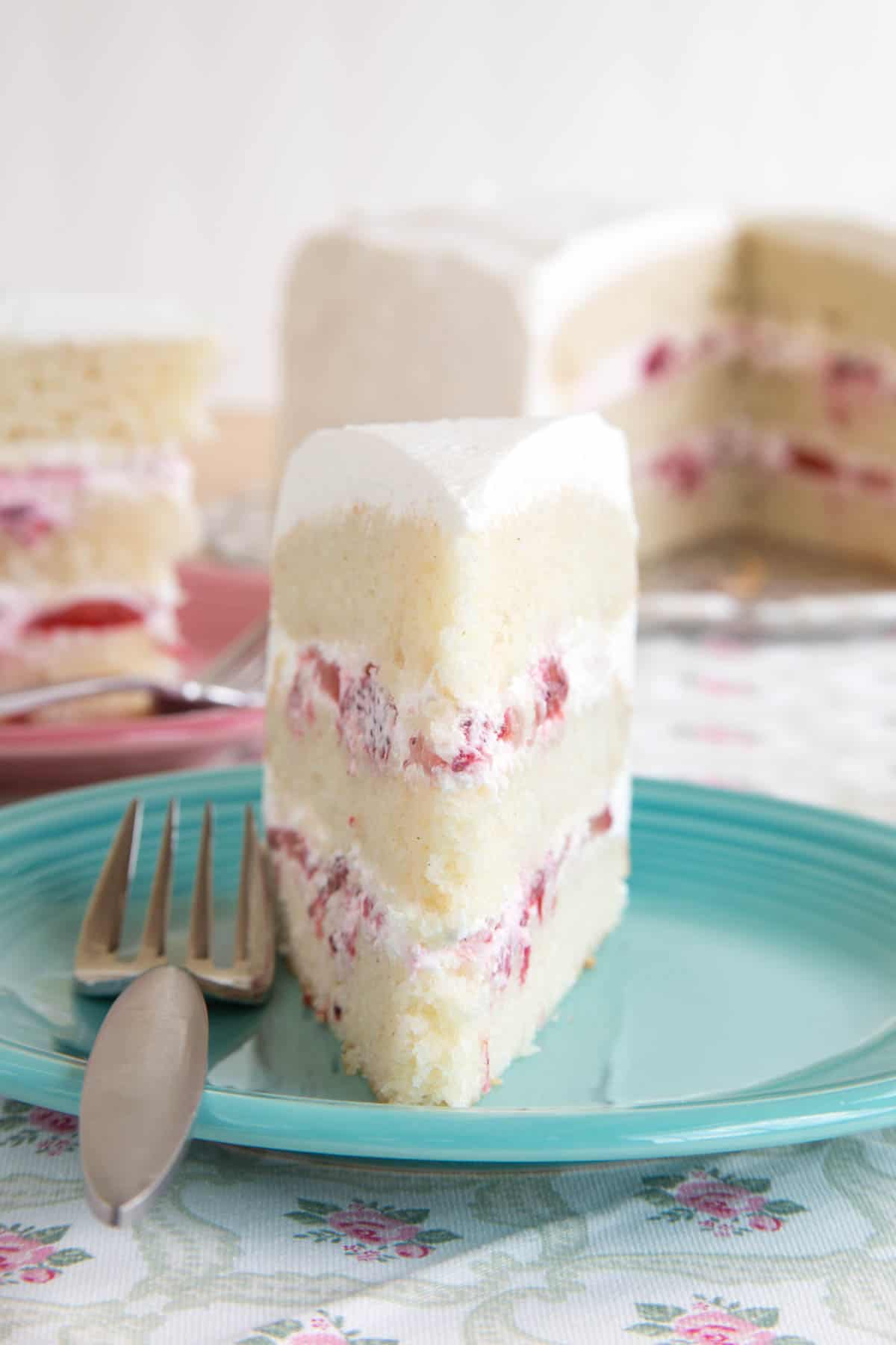 Looking at the front tip of a slice of white gluten free cake with fresh strawberries and whipped cream between the layers.