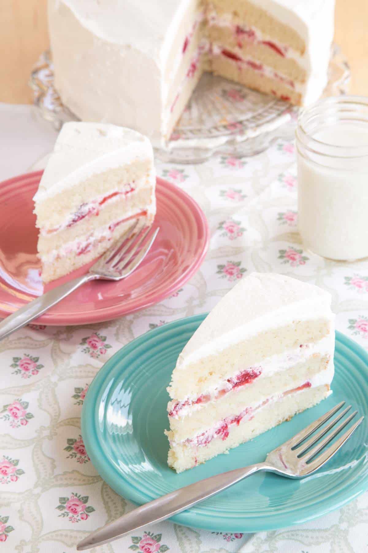 Two pieces of cake on plates on top of a tablecloth with pink roses.