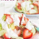 An iceberg lettuce wedge on a pink plate topped with strawberries, cucumbers, bacon, and blue cheese dressing with text overlay that says "Strawberry Wedge Salad".