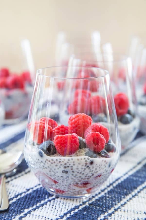 A single glass with a Triple Berry Coconut Chia Seed Parfait and more parfaits in the background